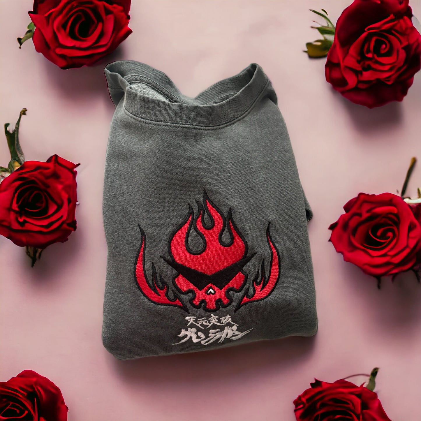 Team Dai-Gurren embroidered crew neck with a red and black flame design on it, displayed against a pink background with rose petals around.