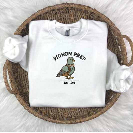 Embroidered crewneck sweater featuring a preppy pigeon in a soft cottagecore aesthetic on a cozy, pastel-colored fabric.