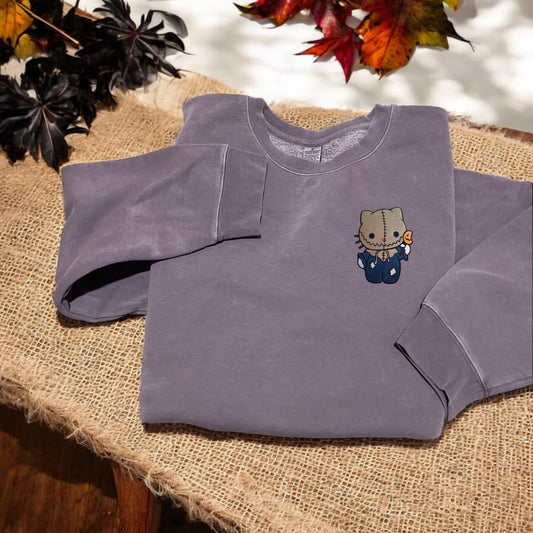 A purple embroidered sweatshirt with a character from Hello Kitty dressed up as a Scarecrow
