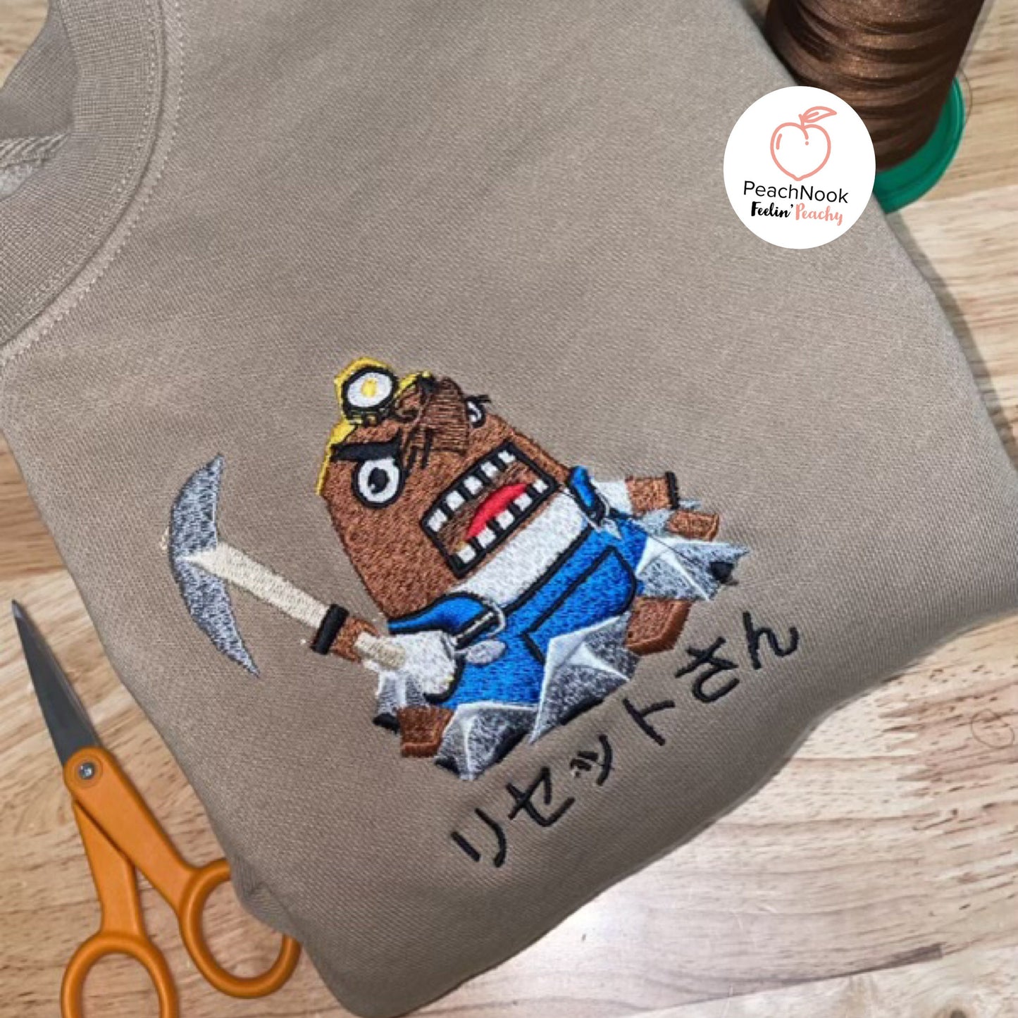 A beige hoodie with an embroidered Resetti from Animal Crossing on the front