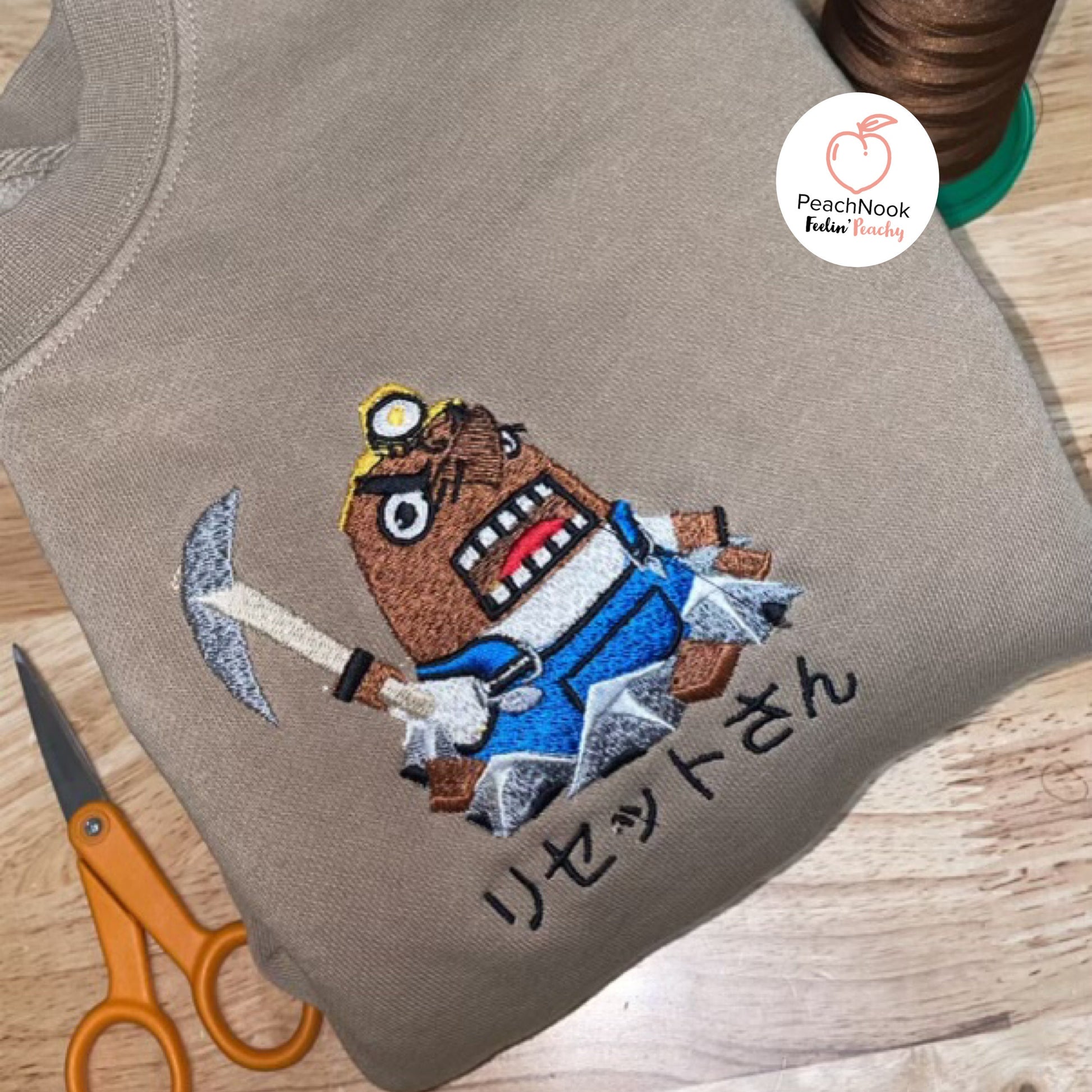 A beige hoodie with an embroidered Resetti from Animal Crossing on the front