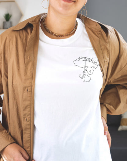 A person wearing a beige jacket and a white t-shirt with a graphic of a kitten holding an umbrella.