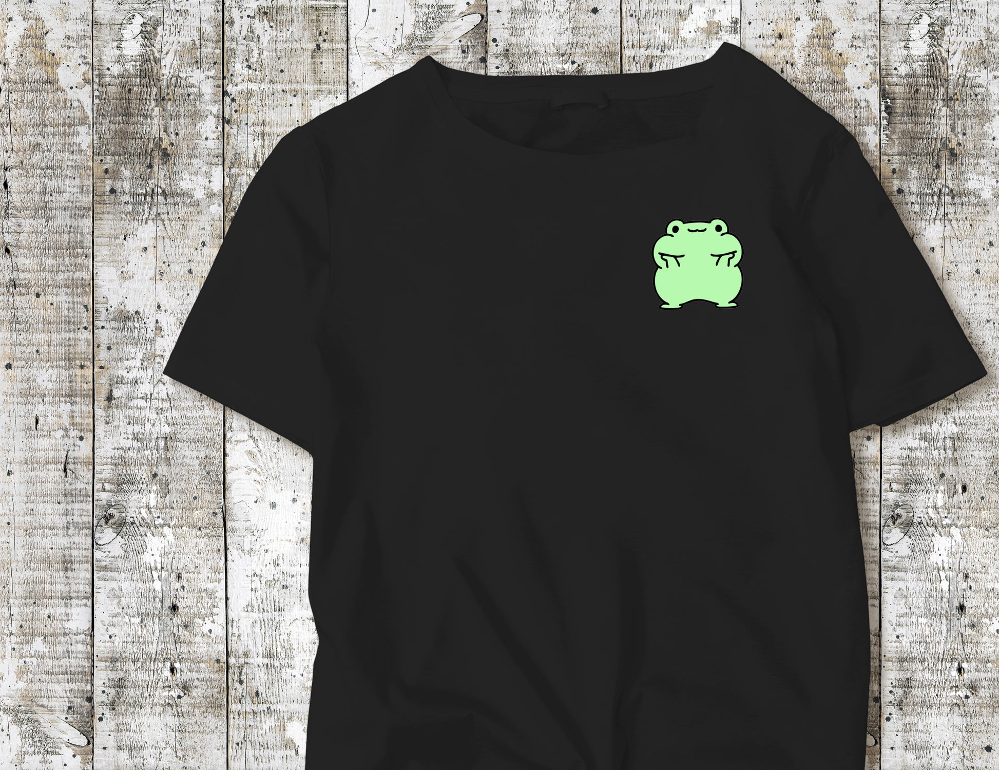 A Green Frog holding his face up on a Black-Tshirt