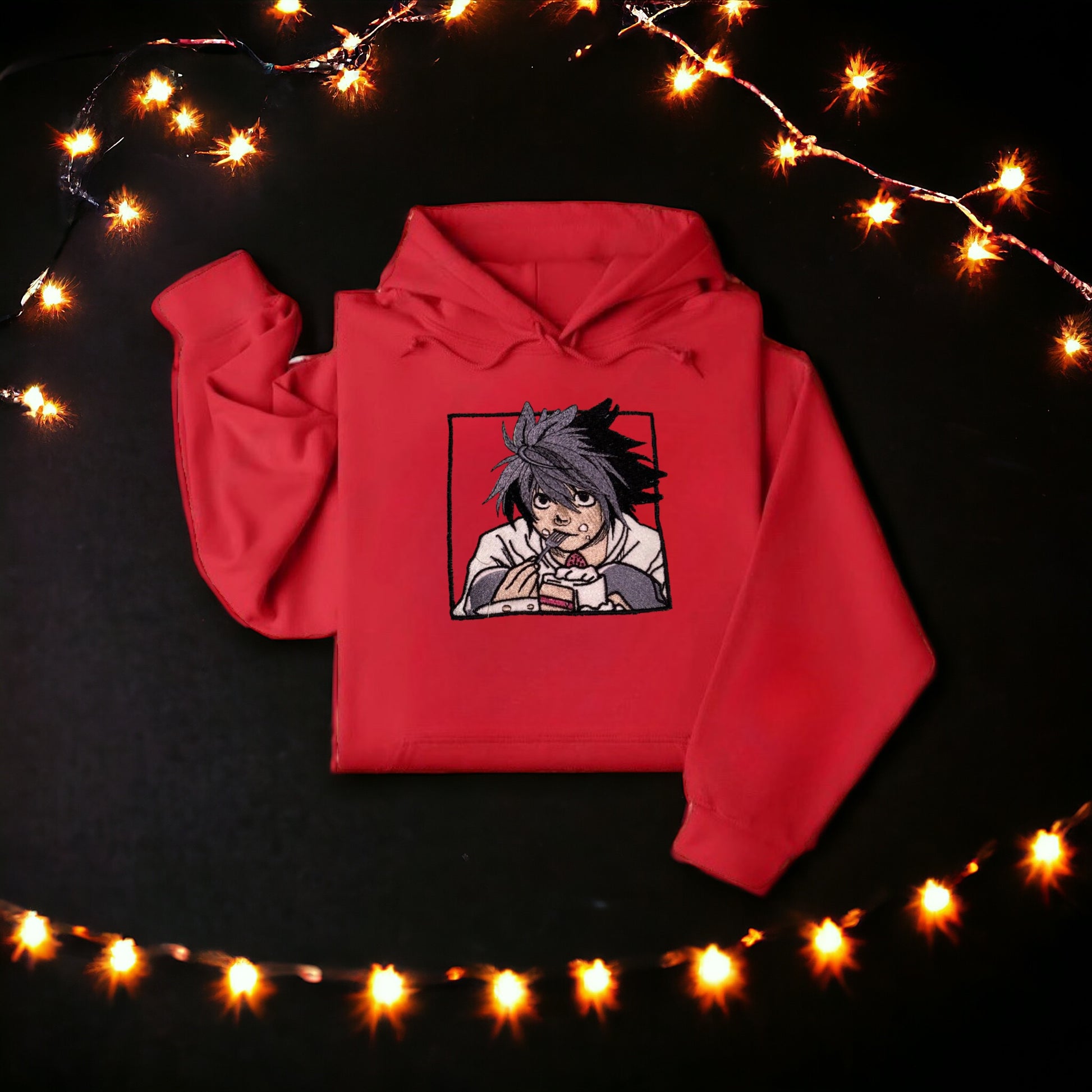 A character named L from the Anime Series, "Death Note' is on a red embroidered hoodie eating cake. 