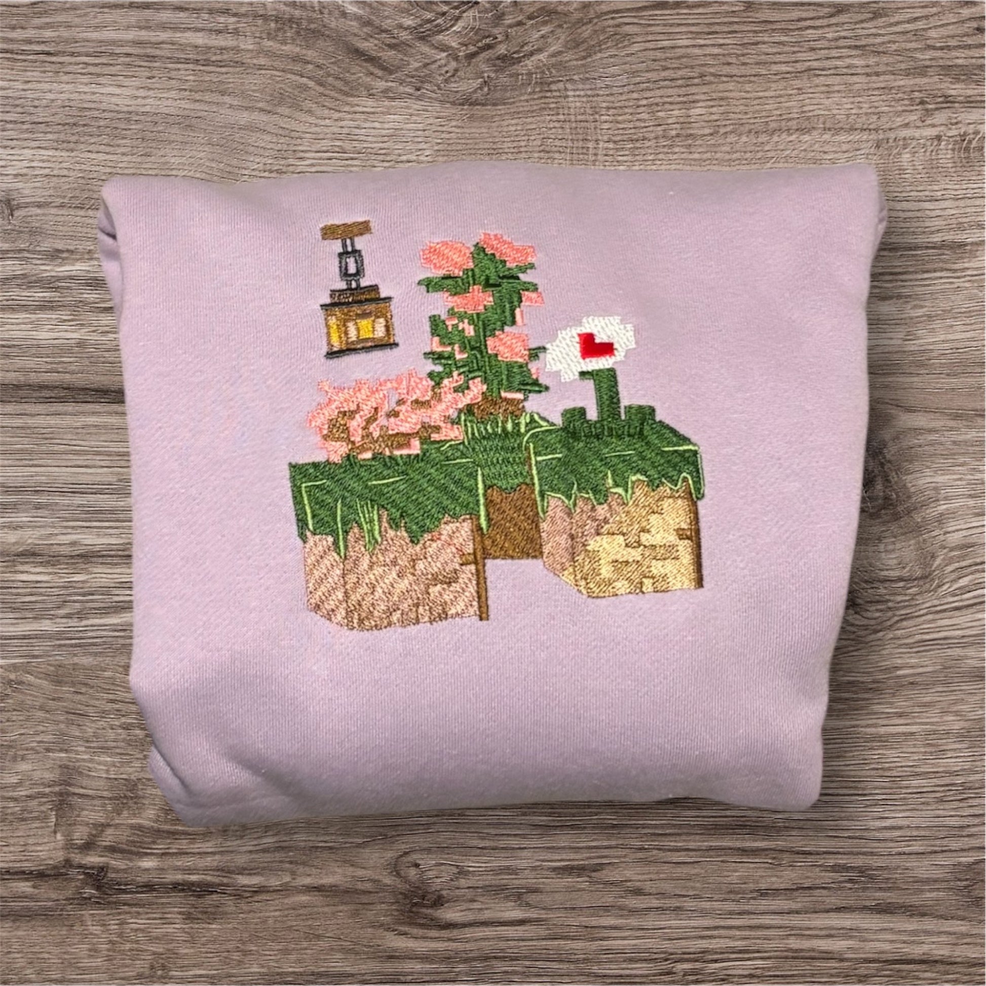 A pink sweatshirt with a graphic design featuring elements from the video game Minecraft, including flowers.