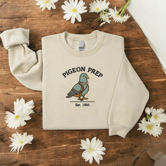 Embroidered crewneck sweater featuring a preppy pigeon  in a soft cottagecore aesthetic on a cozy, pastel-colored fabric.
