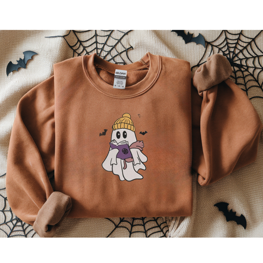 Brown sweatshirt with a ghost wearing a yellow beanie and purple scarf design on a Halloween-themed background.