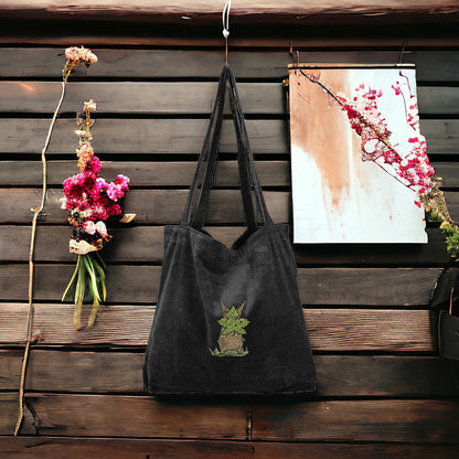 A Black Embroidered Tote bag that has a character from Zelda named Korok  