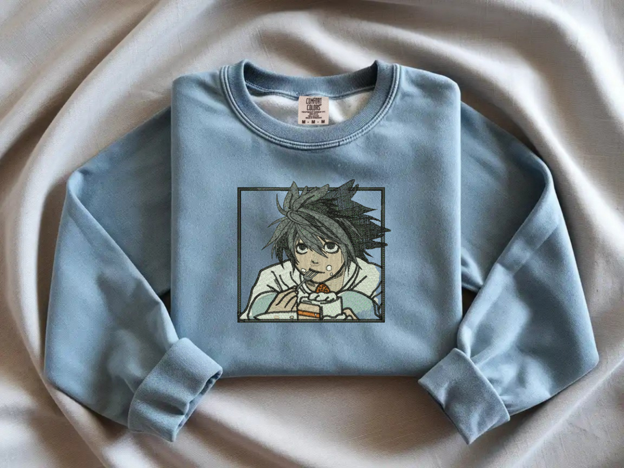 Blue Jeans Comfort Colors crewneck sweatshirt with minimalist black line embroidery of L from Death Note crouching eating cake.