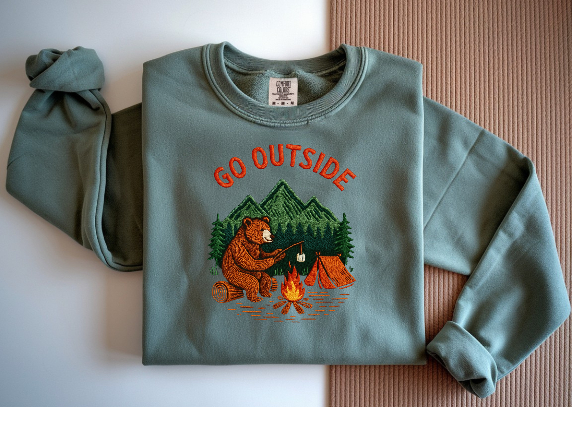 Camping bear embroidered blue spruce crew neck sweatshirt featuring a bear roasting marshmallows by a campfire, cozy outdoor apparel for nature lovers.