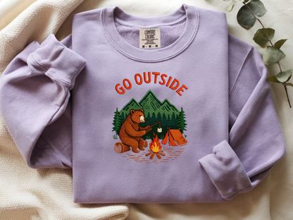 Camping bear embroidered orchid crew neck sweatshirt featuring a bear roasting marshmallows by a campfire, cozy outdoor apparel for nature lovers.