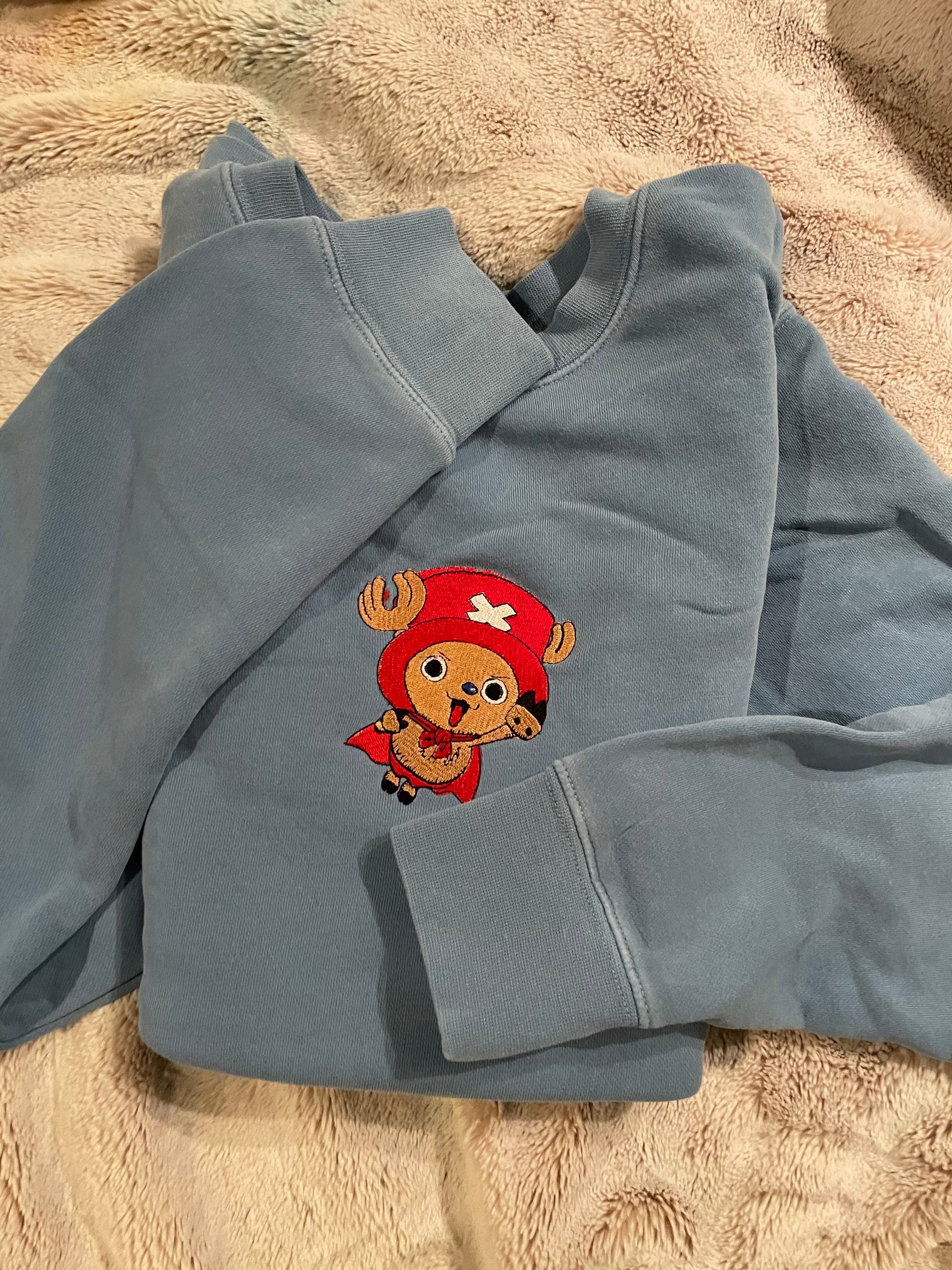 Blue sweatshirt with an embroidered image of Tony Tony Chopper in a red and white outfit on the front.